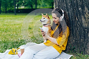 Woman using smartphone listening to music in headphones in green park with dog