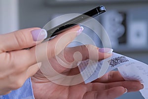 Woman using smartphone and scanning qr code on cash shop receipt paper - closeup