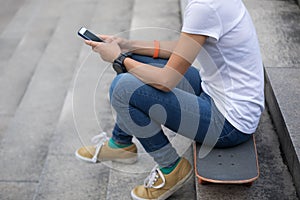 Woman using smartphone sit on skateboard