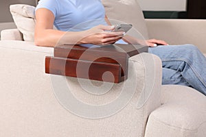 Woman using smartphone on sofa armrest wooden table at home, closeup