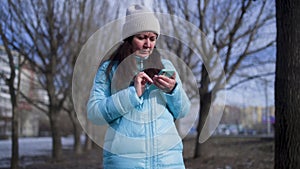 Woman using smartphone while standing against bare trees at park