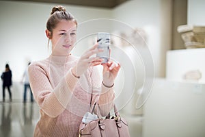 woman using smartphone and standing in art museum