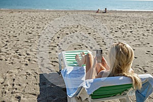 Woman using smartphone while sunbathing on deck chair at empty beach