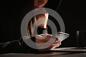 Woman using smartphone at table with laptop in darkness. Loneliness concept