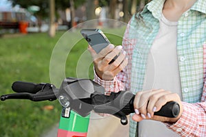 Woman using smartphone to pay and unblock electric kick scooter outdoors, closeup photo