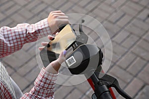 Woman using smartphone to pay and unblock electric kick scooter outdoors, closeup photo