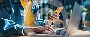 The woman using a smartphone while working on her laptop in a cafe..AI generated image
