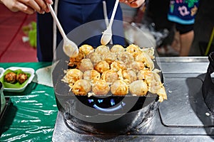 a woman using spoons to cook Takoyaki or a ball-shaped Japanese snack on a black pan