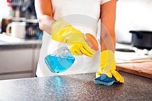 Woman Using Spray Polish To Clean Kitchen Surface