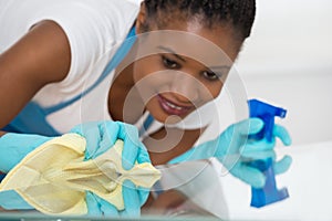 Woman Using Spray To Wipe Glass Desk