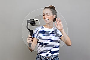 Woman using steadicam and cell phone for livestream, waving hand to followers, saying hi.