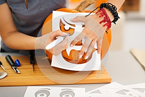 Woman using stencils to carve pumpkin Jack-O-Lantern. Closeup photo