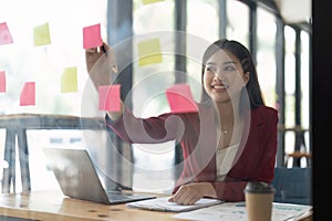 A woman using a sticky note and analysis data report during writing make note some data on notepad, Business financial