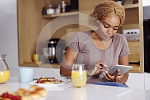 Woman using tablet computer while eating breakfast at home