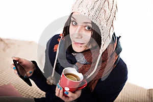 Woman using tablet at cozy home atmosphere on the bed. Young woman with cup tea or coffee in hands enjoying free time