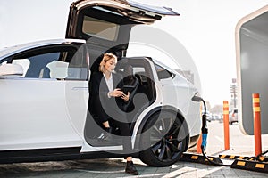 Woman using tablet during electric car charging outdoors
