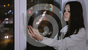 Woman using tablet for video chat and a laugh. Sitting at night on the windowsill in the dark. Scowl