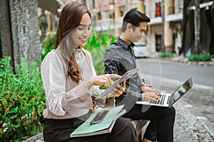 woman using tablet with Young man sitting on the park bench with laptop