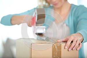 woman using tape dispenser to seal cardboard box