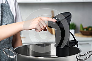 Woman using thermal immersion circulator in kitchen, closeup. Sous vide cooking