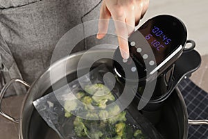 Woman using thermal immersion circulator in pot with broccoli, closeup. Sous vide cooking