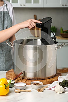 Woman using thermal immersion circulator at table in kitchen, closeup. Sous vide cooking