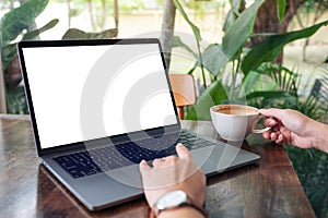 A woman using and touching laptop touchpad with blank white desktop screen while drinking coffee