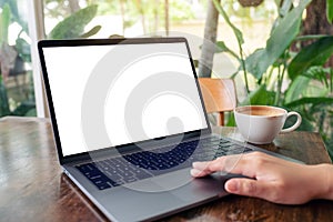 A woman using and touching laptop touchpad with blank white desktop screen while drinking coffee on wooden table