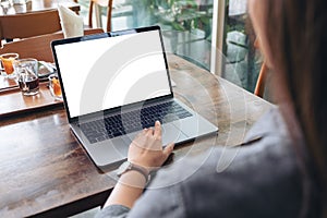 A woman using and touching laptop touchpad with blank white desktop screen on wooden table in cafe