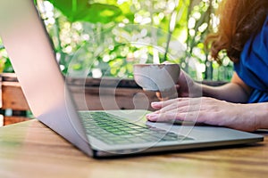 A woman using and touching on laptop touchpad while drinking coffee