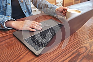 A woman using and touching on laptop touchpad on wooden table while drinking coffee