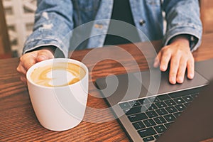 A woman using and touching on laptop touchpad on wooden table while drinking coffee