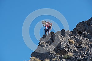 Woman Using Trekking Poles To Descend Steep Rock