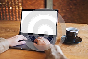 A woman using and typing on laptop with blank white desktop screen with coffee cup on the table