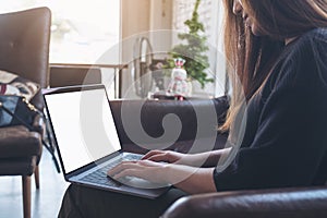 A woman using and typing on laptop with blank white desktop screen on sofa in cafe