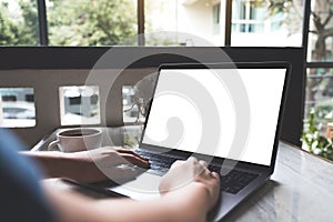 A woman using and typing on laptop with blank white screen and coffee cup on table in modern cafe