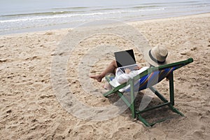 A woman using and typing on laptop computer on a beach chair