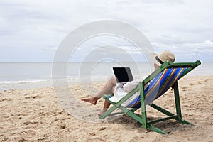 A woman using and typing on laptop computer on a beach chair