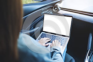 A woman using and typing on laptop computer with blank desktop screen in the car