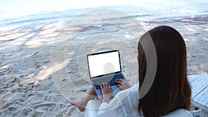 A woman using and typing on laptop computer with blank desktop screen while sitting on the beach