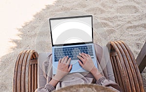 A woman using and typing on laptop computer with blank desktop screen while sitting on the beach