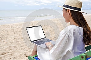 A woman using and typing on laptop computer with blank desktop screen while sitting on a beach chair