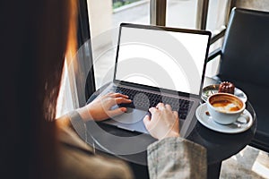 A woman using and typing on laptop computer with blank white desktop screen in cafe