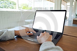 A woman using and typing on laptop computer keyboard with blank white desktop screen on wooden table