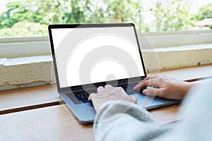 A woman using and typing on laptop computer keyboard with blank white desktop screen on wooden table