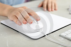 Woman using wired computer mouse on pad at grey marble table, closeup