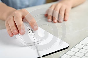 Woman using wired computer mouse on pad at grey marble table, closeup