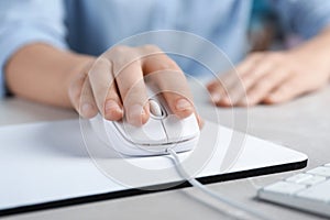 Woman using wired computer mouse on pad at grey marble table, closeup