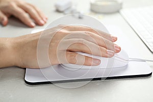 Woman using wired computer mouse on pad at light grey marble table