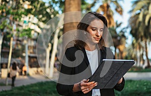 Woman using wireless earphones selects music holding laptop computer while relaxing Park in Barcelona, successful girl manager